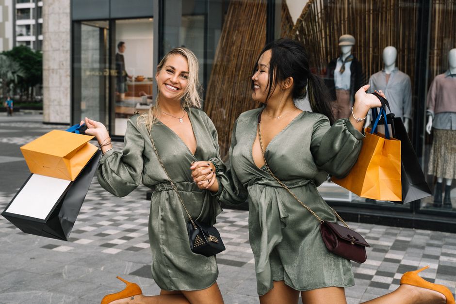 Two smiling friends enjoy a day of shopping with bags in hand outside a stylish boutique.